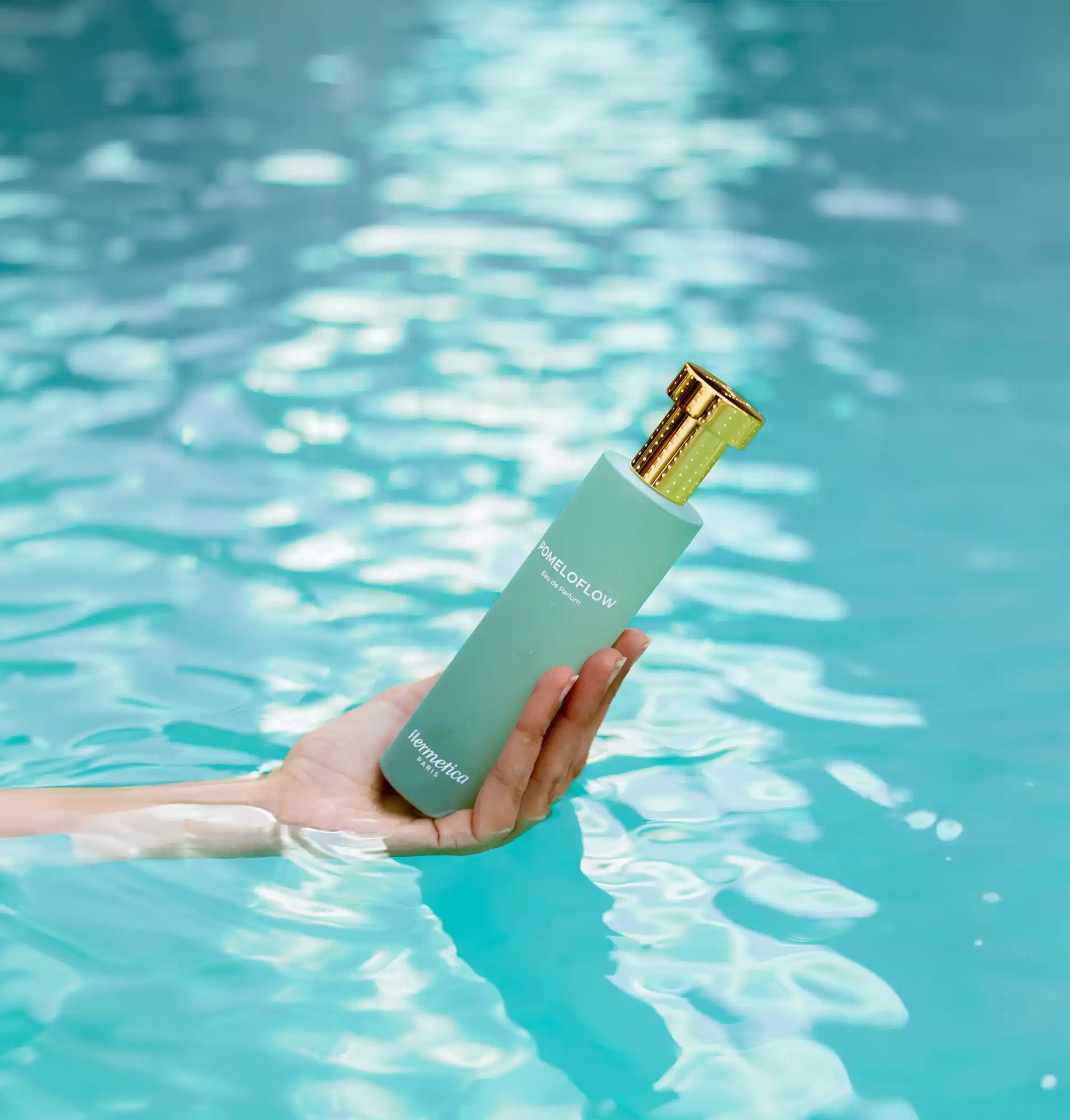 Turquoise glass bottle with a gold cap being held above water.